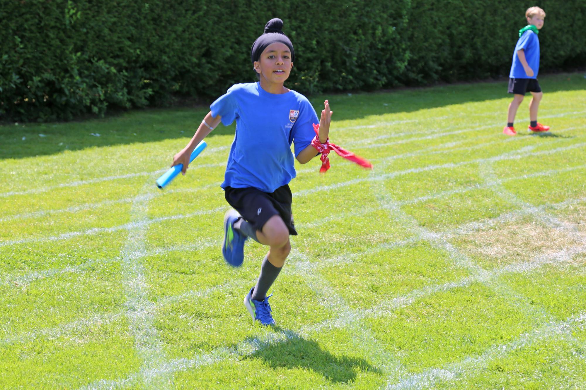 A student participates in a track and field relay -- running and carrying a baton -- during Sports Day at the Junior School.
