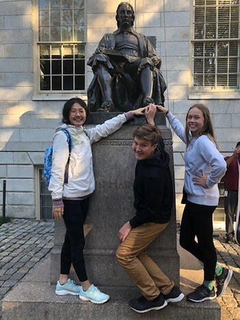 Three debate club students standing in front of a statue