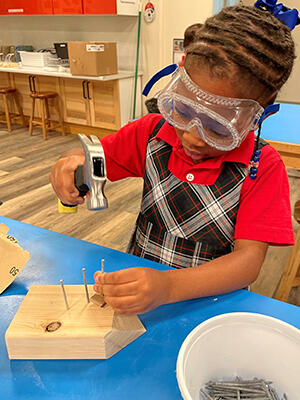 A student hammers a nail in the process of making a hedgehog