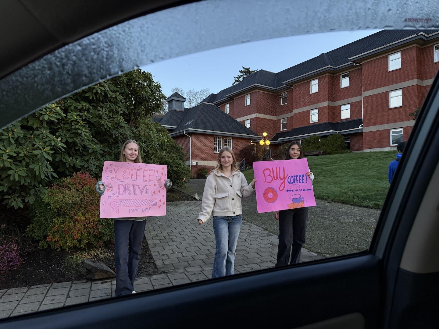 Three students hold coffee drive signs