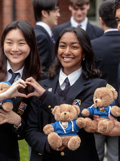 Three Senior School students pose holding their grad teddy bear with two of the female students making a heart together with their hands.