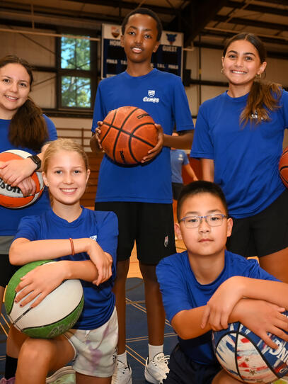 Group of five players taking a staged photo holding Basketballs
