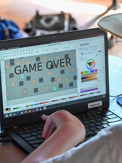 Game Development Camper playing the game they have made with "game over" on the laptop screen