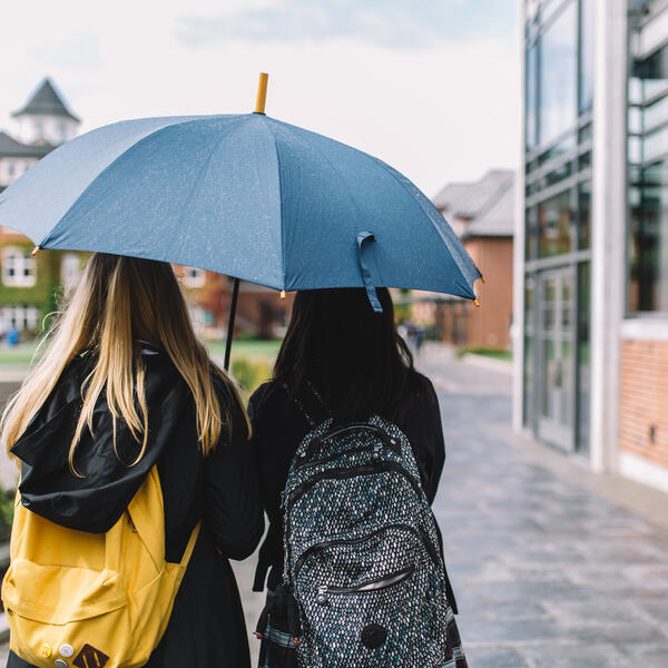 Two students walking through campus under an umbrella