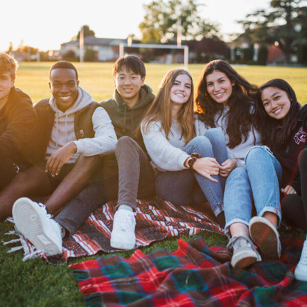 Group of happy Senior School students sitting on a blanket in the field