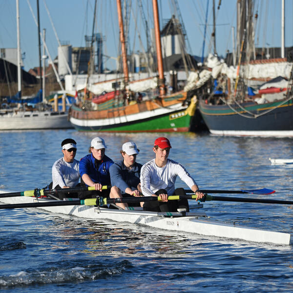 A men's quad rows on the Gorge waterway in front of some boats.