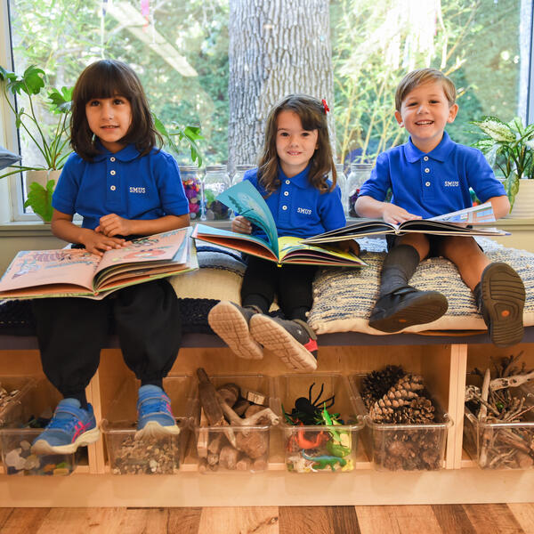 A group of Junior Kindergarten students smile while reading in the classroom