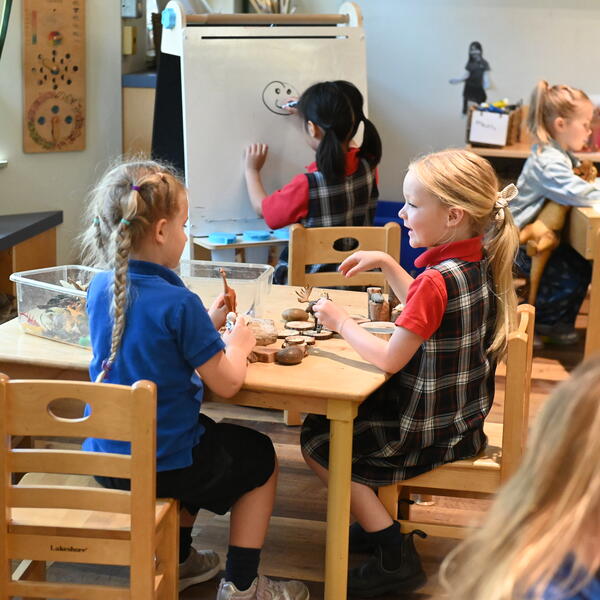 Two young students sit at a table together interacting and playing.