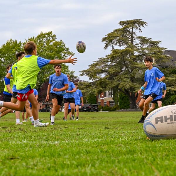 Group of campers playing rugby with a rugby ball in the front of the frame