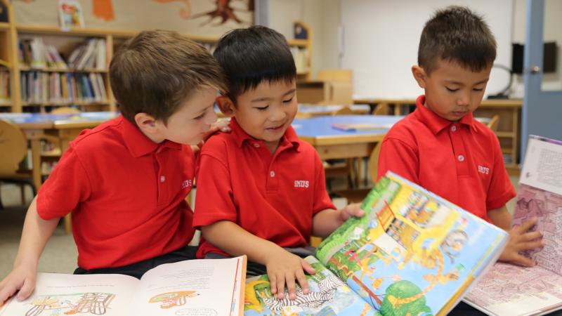 Three Kindergarten students read colourful picture books together in the library.