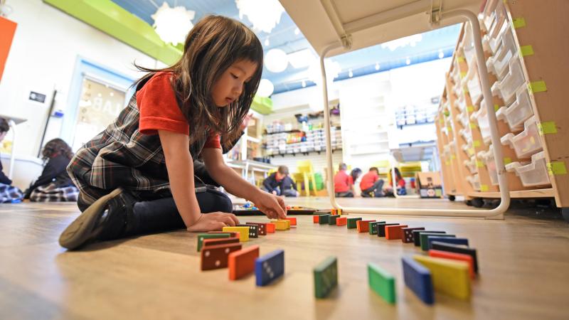 A Kindergarten student lines up dominoes while sitting underneath a table in the Imagination Lab.