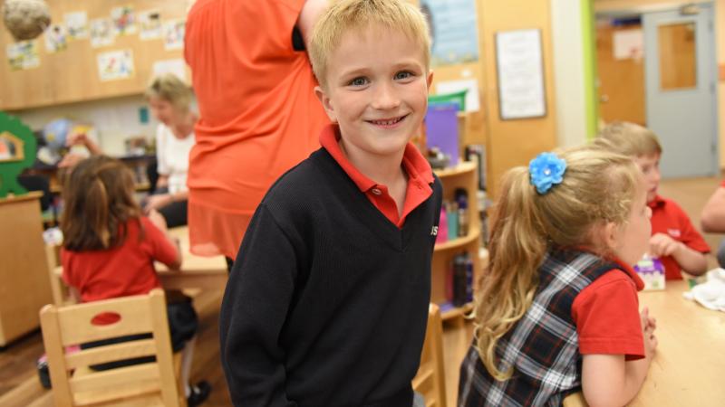 A Kindergarten student smiles for a photo while standing in the classroom.