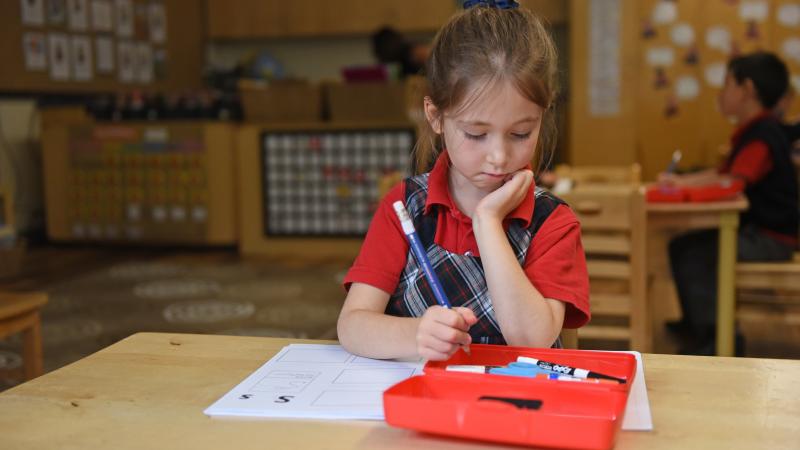 A Kindergarten student sits at a desk while completing a writing assignment.