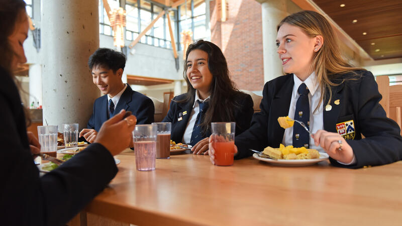 Three Senior School boarding students sit at a table in a dining hall eating a meal.