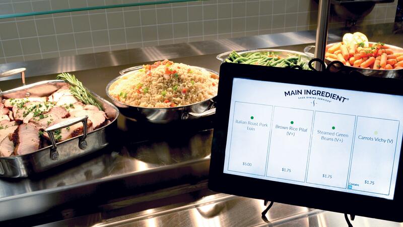 A digital menu screen is on display in front of a buffet of colourful, fresh and hot looking food.