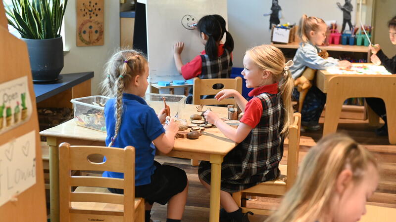 Two young students sit at a table together interacting and playing.