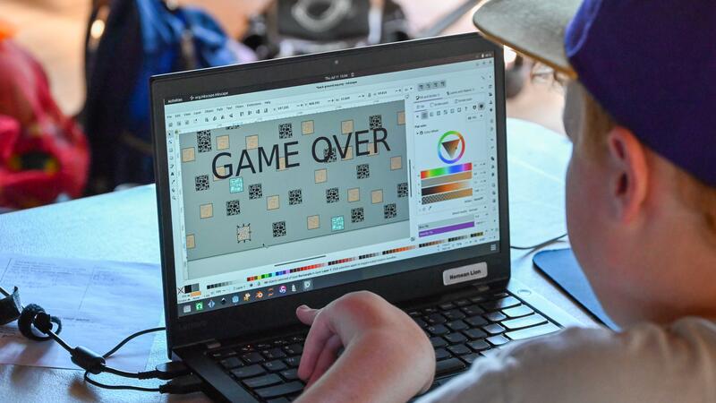 Game Development Camper playing the game they have made with "game over" on the laptop screen