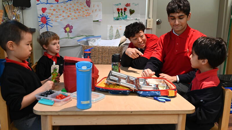 Two Lifers sit with current Kindergarten students during snack time