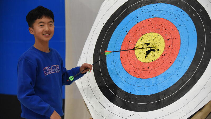 A student smiles with an arrow in a target