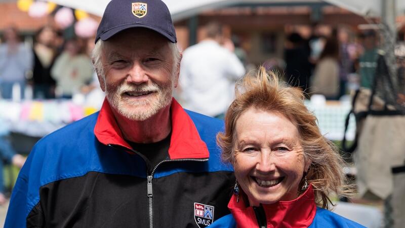 Two alumni in retro SMUS jackets smile over 2025 Alumni Weekend