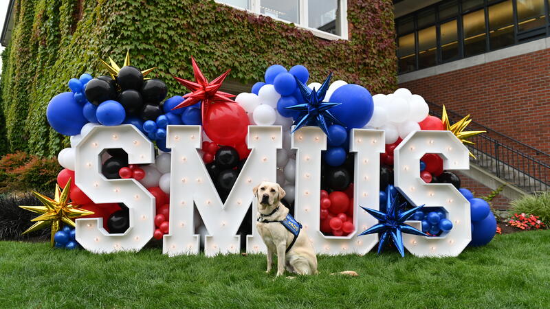 Radar the Accredited Facility Dog poses in front of giant SMUS decorated letters