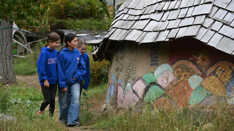 Grade 6 students walk up a path admiring the Ecovillage Dragon Wall with artwork from generations of SMUS students