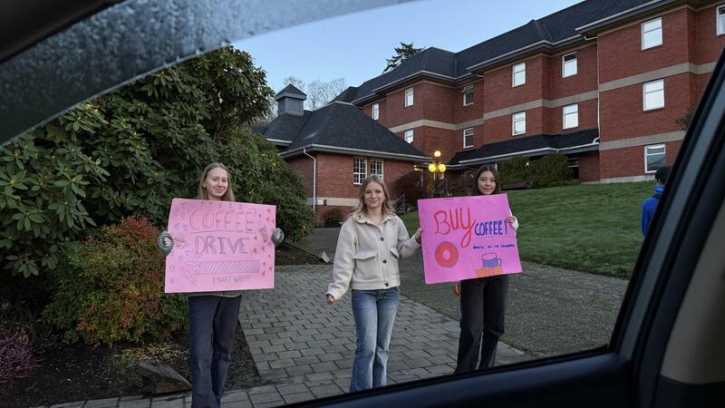 Three students hold coffee drive signs