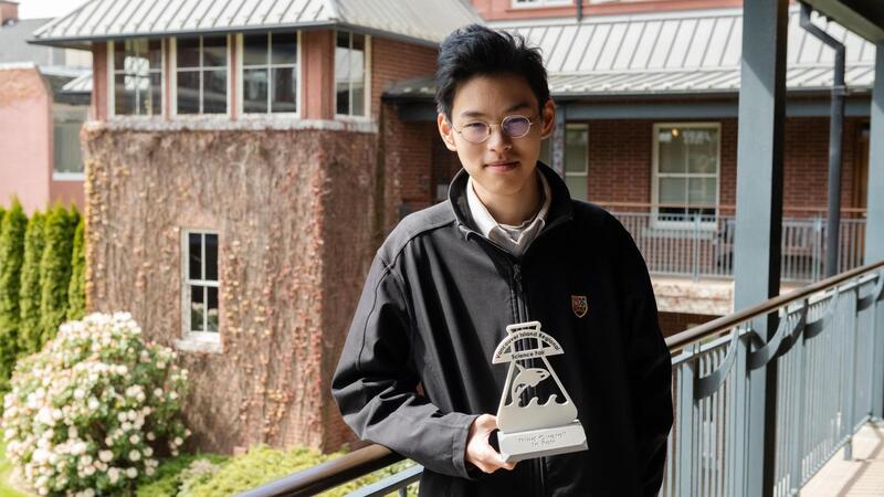 George Wang leans on a railing onlooking SMUS campus while holding his 3D printed Science Fair trophy
