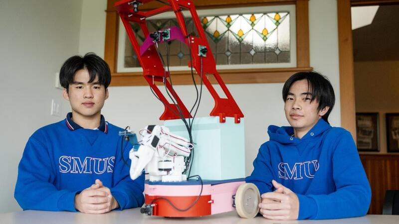 Edmond Aphiwetsa and Sting Zhang pose beside their 3D printed device that is an automatic garbage picker upper. 