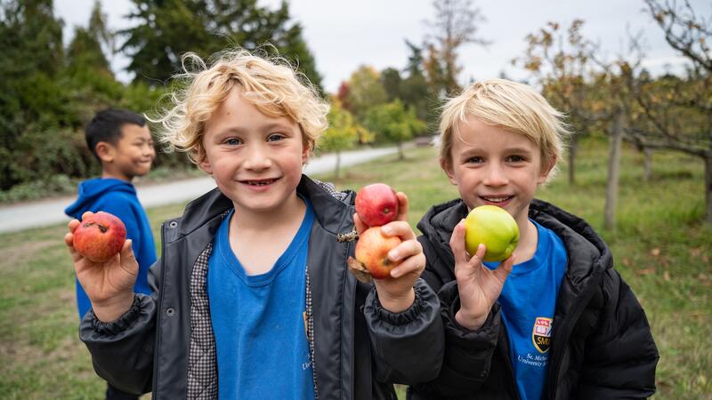 Two students smile holding up apples.