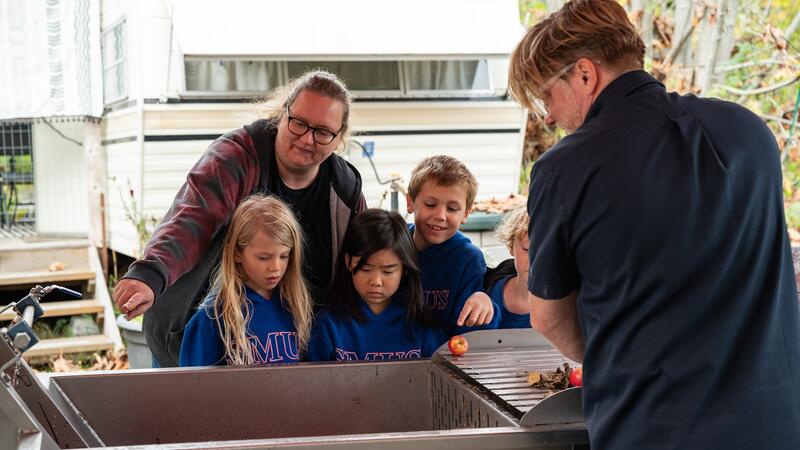 Three students look on as a staff member explains some machinery they use to process apples.