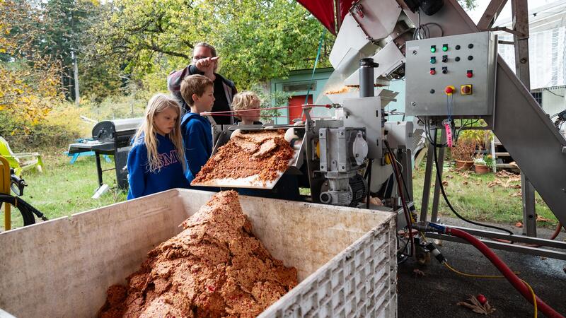 Three students look on as a staff member explains some machinery they use to process apples.