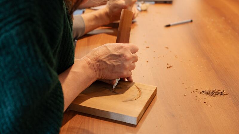 Close up of hands holding a knife while carving cedar