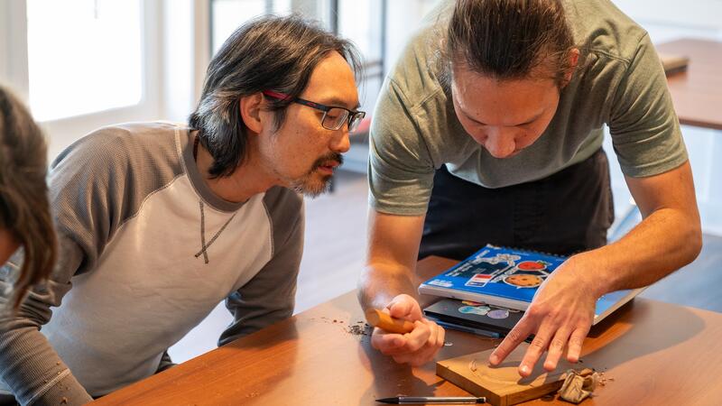 Dylan Thomas demonstrates a carving technique as Lawrence Wong looks on