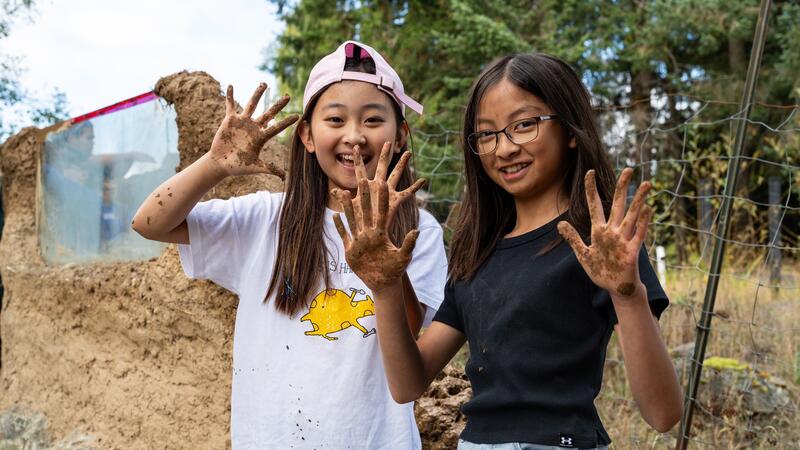 Two students pose with their muddy hands up with the man-made dragon wall in the background.