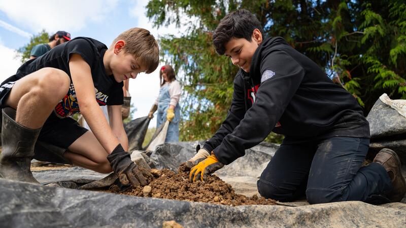 Students pack dirt with their hands on a tarp. 